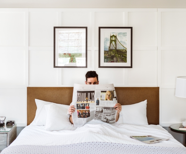 A man reading the paper in bed in his suite at the Heathman Hotel in Portland, Oregon.