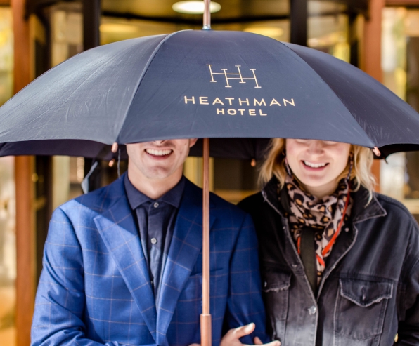 A couple standing under a Heathman Hotel umbrella.