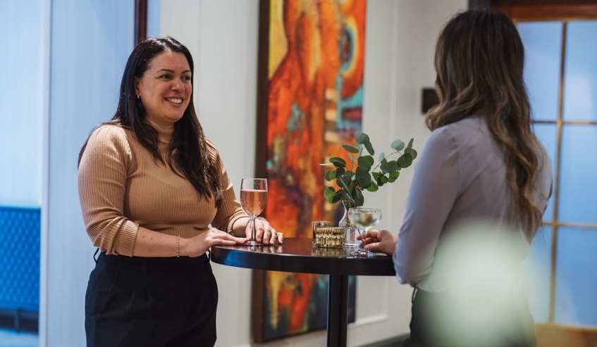 Two women standing at a bar table having drinks.